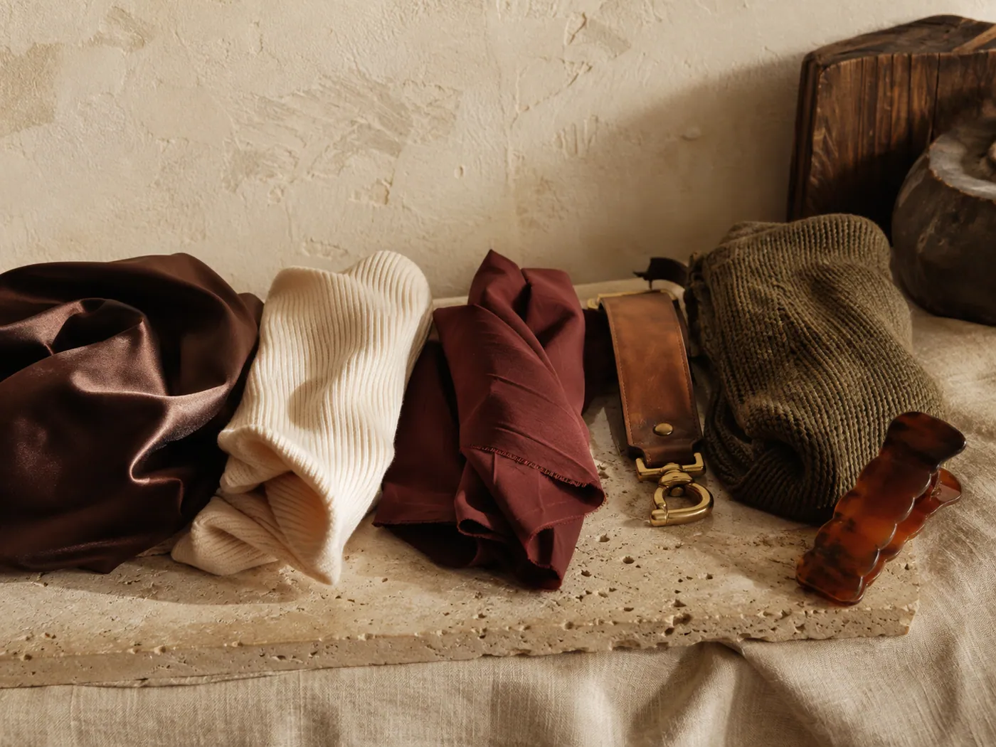 Separated piles of satin, cotton rib knit, nylon twill, vegan leather with brass hardware, wool-blend knit and a resin clip