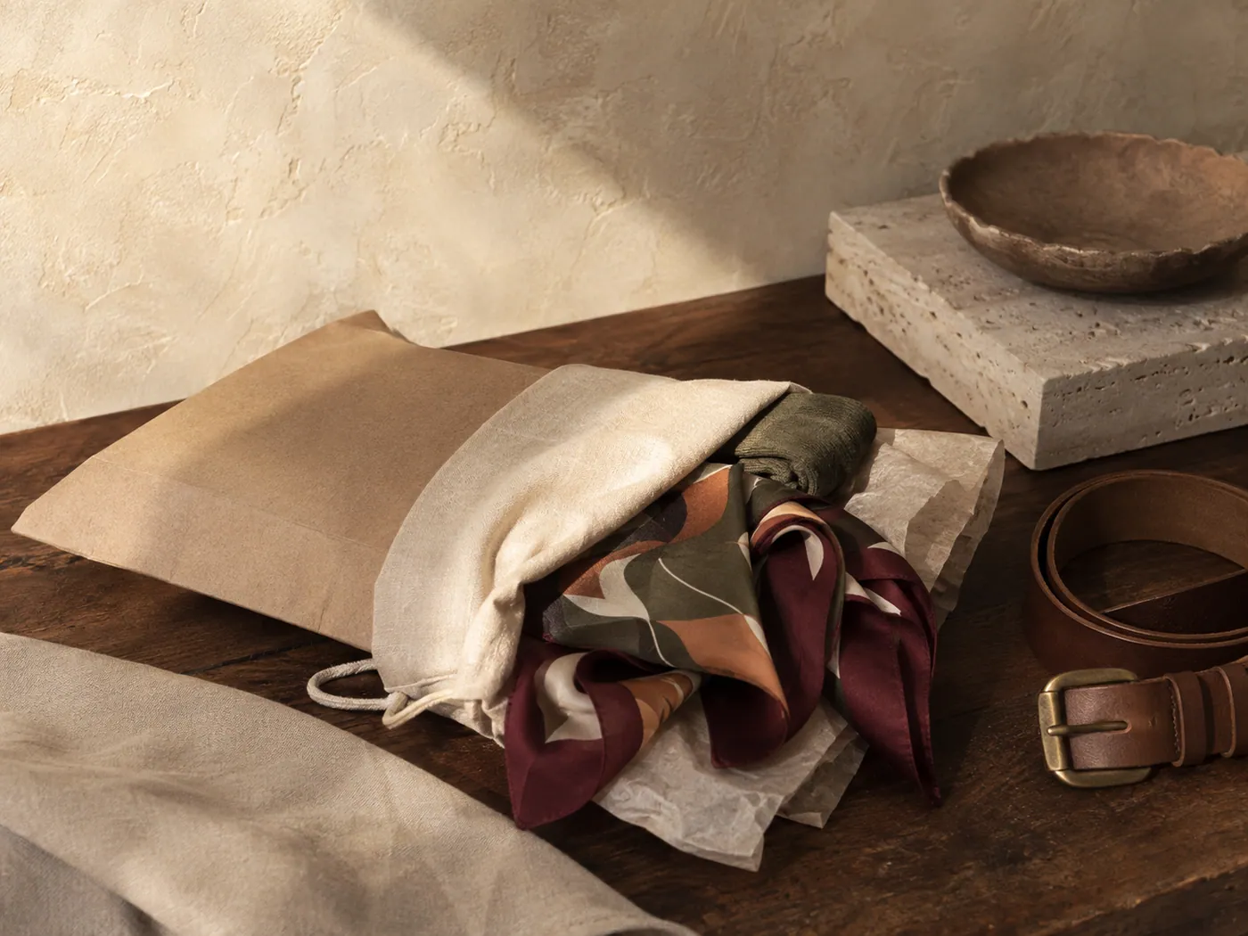 A kraft mailer, cotton dust pouch and tissue with a headscarf, socks and a belt ready to post